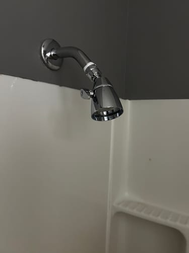 Reviewer's shiny chrome 2 Inch Shower Head installed in their shower against a grey wall.