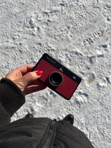 Eine Kundin hält die rote, handliche NUVINT Digitalkamera in der Hand, mit Schnee im Hintergrund.
