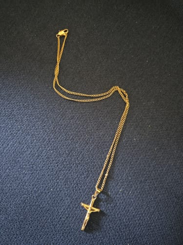 Reseña de cliente del colgante Cross Minimal Pendant Oro, mostrando la cadena y el crucifijo dorado sobre una tela azul.