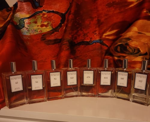 Reviewer's collection of perfumes on a shelf, featuring the 'Inspired by Good Girl - 81' bottle among others.