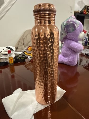 Customer's hand-hammered Pure Copper Water Bottle standing on a paper towel on a wooden table.