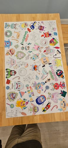 Customer's Christmas Monsters table size coloring sheet spread on a wooden table, partially filled in with bright colors.