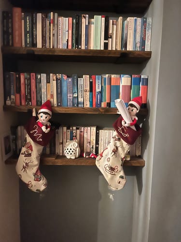 Customer's two Christmas stockings made from the printed fabric, hanging from a bookshelf with elves inside.