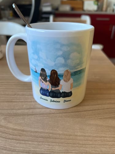 Kundin zeigt ihre personalisierte 'Beste Freundinnen'-Tasse, die drei Frauen am Strand und individuelle Namen abbildet.
