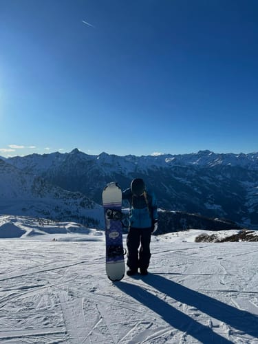 Reviewer wearing the baggy snow pants while standing with a snowboard on a mountain.