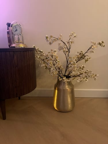 Recensent toont de witte Zijden Bloesems in een glanzende gouden vaas op een houten vloer.