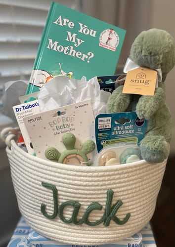 Customer's white knitted basket personalized with the name 'Jack' in green yarn, used as a gift basket for baby items.