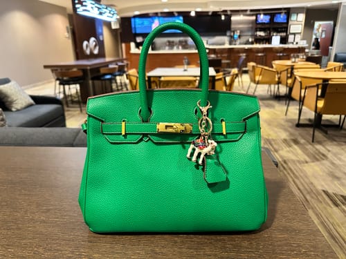 Customer's bright green LALUVA Warkin Bag with a zebra charm sitting on a table in a restaurant.