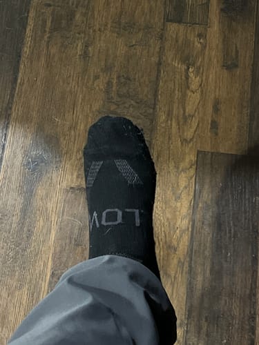 Customer wearing a black alpaca sock with grey details on a wood floor, seen from above.