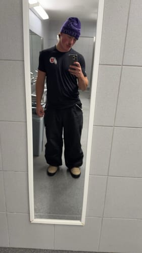 Reviewer taking a full-length mirror selfie while wearing the black baggy snow pants.