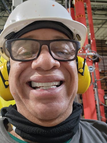Close-up of a reviewer smiling, showing a full, white set of Pop On Veneers while wearing a hard hat.