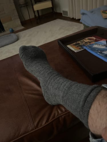 Customer wearing the comfortable, grey Men's Alpaca Socks while relaxing with their foot up.
