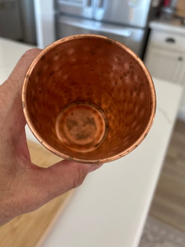 Customer holding the Artisan Hammered Copper Glass, showing dark spots on the hammered interior.