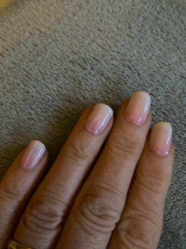 Nahaufnahme der Hand einer Kundin, die ihre fertigen Babyboomer-Nägel nach dem Aushärten mit der UV-LED-Lampe zeigt.
