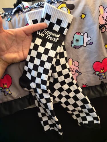 Reviewer's hand holding up a pair of black and white Checkers Crew Socks with 'Speed We Trust' text.