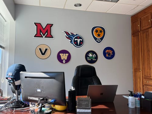 Customer's Miami University 'M' wall art displayed on an office wall with a collection of other team logos.
