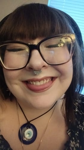 A close-up of a happy customer smiling while wearing the intricate Moth Septum piercing.