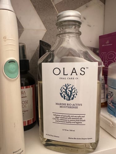 Reviewer's bottle of OLAS Mouthrinse on a bathroom counter next to an electric toothbrush.