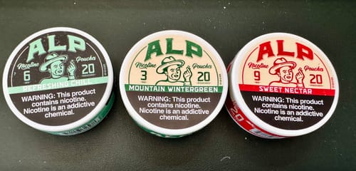 Customer's three tins of ALP nicotine pouches in different flavors and strengths: Refreshing Chill, Mountain Wintergreen, and Sweet Nectar.