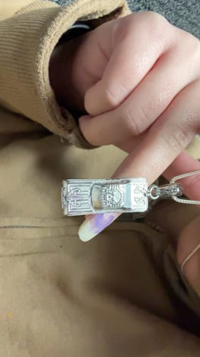 Close-up of a customer holding the intricate silver Lowrider Pendant on its chain against a tan jacket.