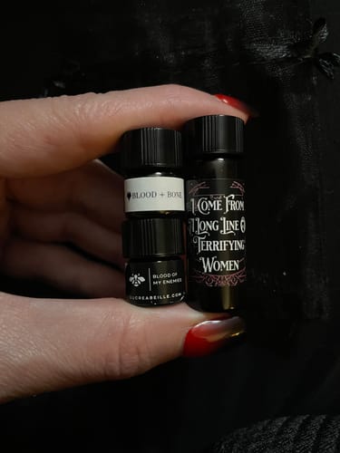 Customer's hand holding small sample vials, including one for the Blood of My Enemies fragrance.