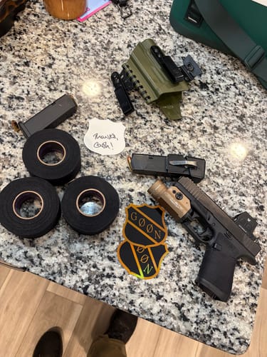 Reviewer's three rolls of Blackout Triple tape on a counter next to a handgun with the tape applied to the grip.