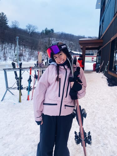 Reviewer in the Rose Multifunctional Snow Jacket standing outside a ski lodge.
