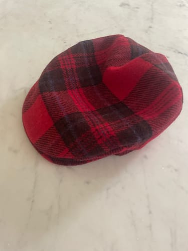 Reviewer's Festive Tweed Cap in a red and black check pattern, shown on a marble surface.