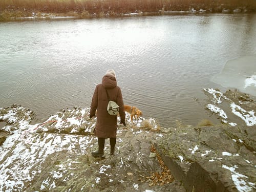 Kundenfoto, aufgenommen mit der NUVINT Digitalkamera. Es zeigt eine Person mit Hund an einem verschneiten, felsigen Flussufer.