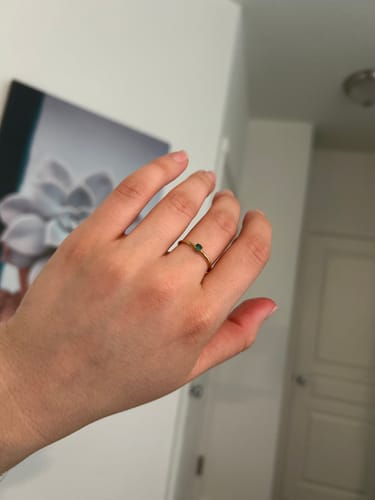Reviewer's hand wearing a minimalist gold Birthstone Ring with a small green crystal.