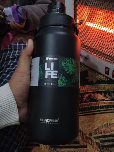 A reviewer holds the large, black D.Kadi Thermal Vacuum Bottle in their hand indoors.