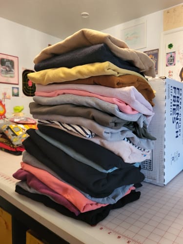 Customer's large, colorful stack of folded Wholesale Blank Sweatshirts on a table next to a shipping box.