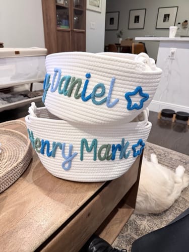 Customer's two personalized white knitted baskets on a table, one with 'Daniel' and the other with 'Henry Mark' in multicolor yarn.