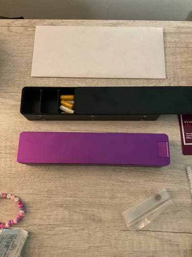 Customer's two Weekly AM-PM Vitamin Cases on a desk. The black case is open with pills inside next to a closed purple case.