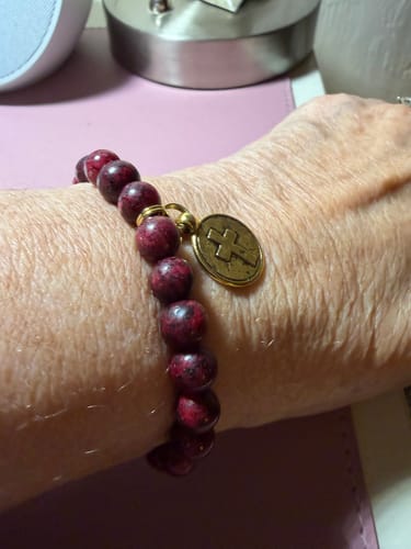 Reviewer wearing the Christmas Bracelet, showing the deep red jasper beads and antique-gold cross charm on their wrist.