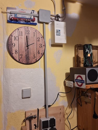 Kundenfoto der Wanduhr aus Holz Nature Love, die in einer Werkstatt an einer gelben Wand hängt.