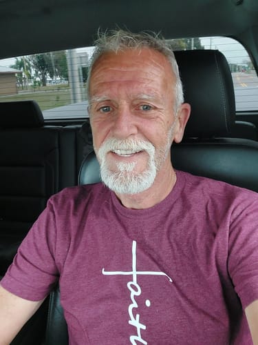 Reviewer smiling while wearing the maroon Faith Cross Tee inside a car.