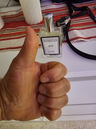 Customer giving a thumbs-up in front of their bottle of 'Inspired by Green Irish Tweed - 411' perfume on a white surface.