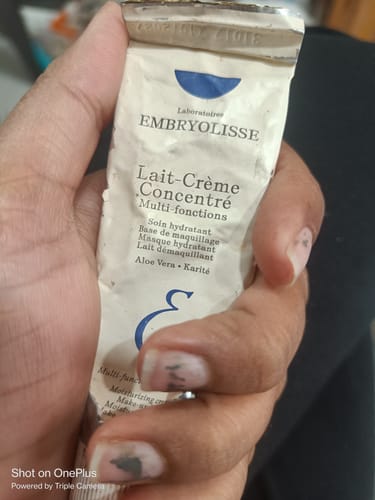 A reviewer holds a well-used, crumpled tube of Embryolisse Lait-Creme Concentre in their hand.