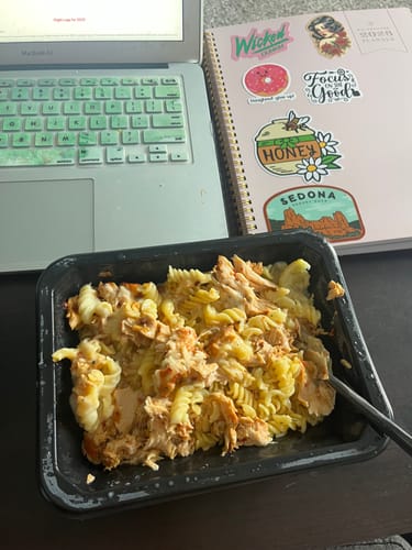 Reviewer's prepared Salmon Alfredo meal with pasta and flaked salmon in its black container on a desk.