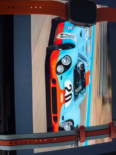 Reviewer's orange Apple Band ULTRA on a watch, shown with another band over a photo of a color-coordinated race car.