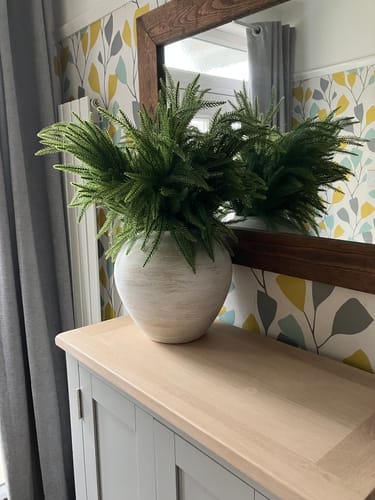 Customer's brushed white Arina Vase filled with green ferns, displayed on a wooden cabinet in a hallway.