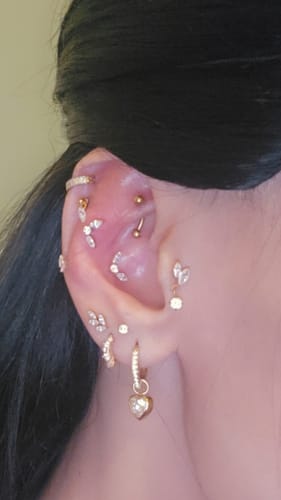 Close-up of the reviewer's ear, showing the dainty Ice Drip flatback Gold earring styled with other gold piercings.