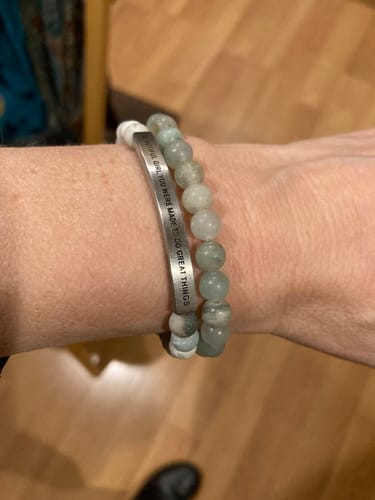A reviewer's wrist wearing the engraved message bracelet next to the matching light green beaded bracelet.