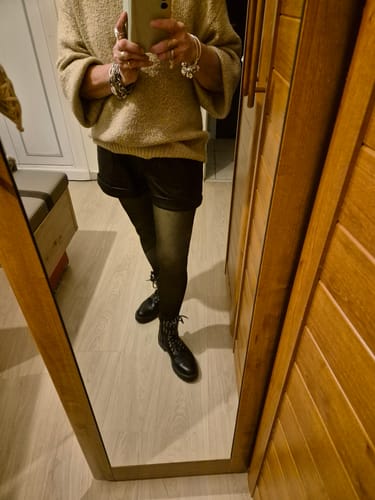 Une cliente prend une photo miroir de sa tenue, portant le collant polaire transparent noir avec un short et des bottines.