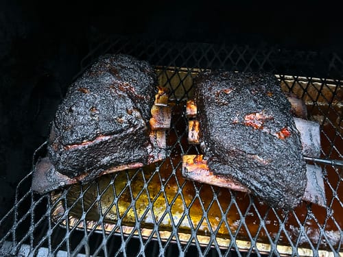 Customer's two plates of Bone-In Short Ribs with a dark, smoked crust resting inside a smoker.