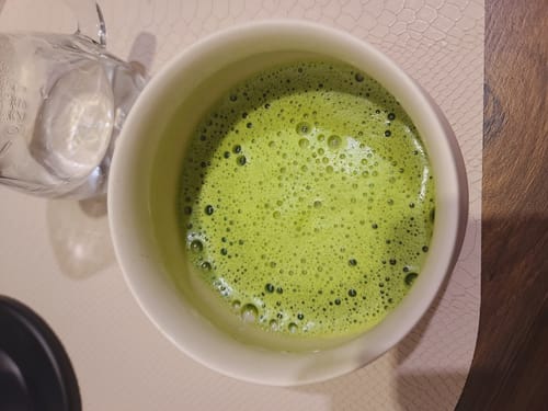 Avis d'un client sur le thé Matcha Cérémonie Bio, vert et mousseux, servi dans un bol blanc.