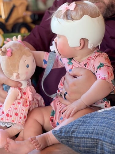 A customer's image of a baby sitting on a lap, holding the Personalized Strawberry Girl doll.