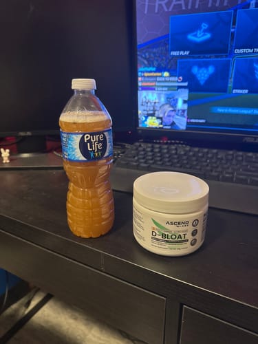 Reviewer's white jar of D-BLOAT next to a water bottle containing the prepared orange-colored drink.