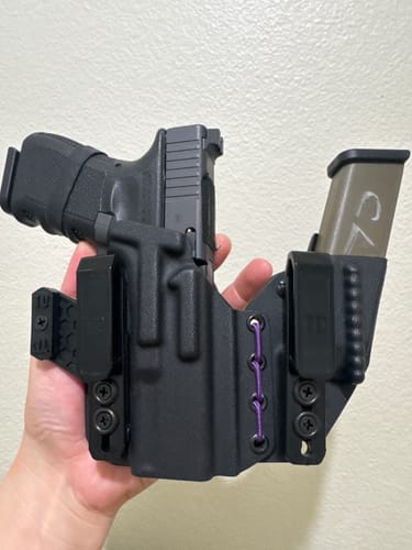 Reviewer holding the black AXIS ELITE holster with a firearm, magazine carrier, and purple shock cord.